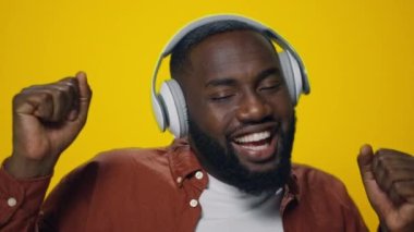 Afrikalı adamın portresi sarı arka planda kulaklıkla müzik dinlemekten zevk alıyor..
