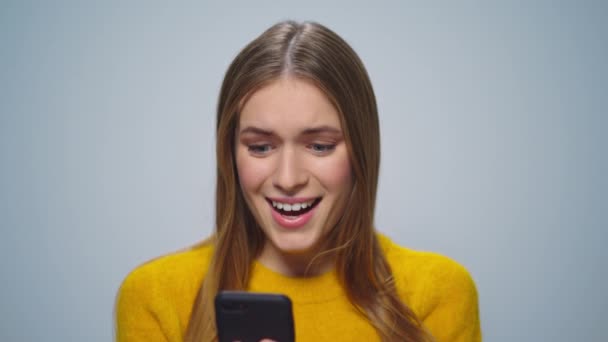 Retrato de mujer sorprendida leyendo buenas noticias en smartphone sobre fondo gris. — Vídeos de Stock