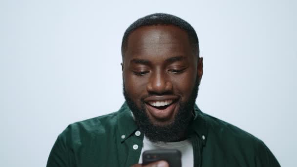 Retrato del hombre africano emocional mirando la pantalla del teléfono inteligente en fondo gris. — Vídeos de Stock