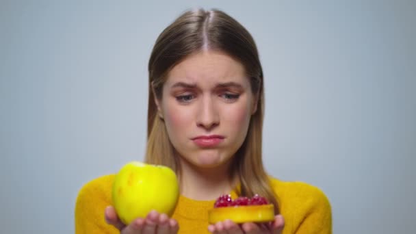 Portrait of thoughtful woman selecting between apple or cake at camera. — Stock Video