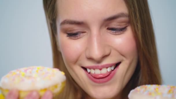 Close-up vrolijke vrouw eten donut met grote eetlust op grijze achtergrond. — Stockvideo