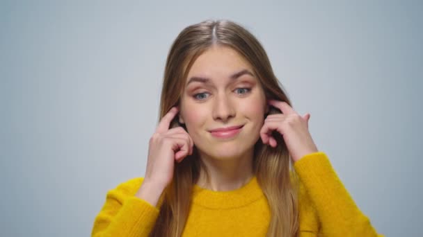 Porträtt av leende kvinna täcker öronen med fingrar framför kameran i studion. — Stockvideo