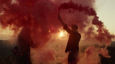 Kadın ve erkek renkli sis bombalarıyla el sallıyor. Çiftler eğleniyor.