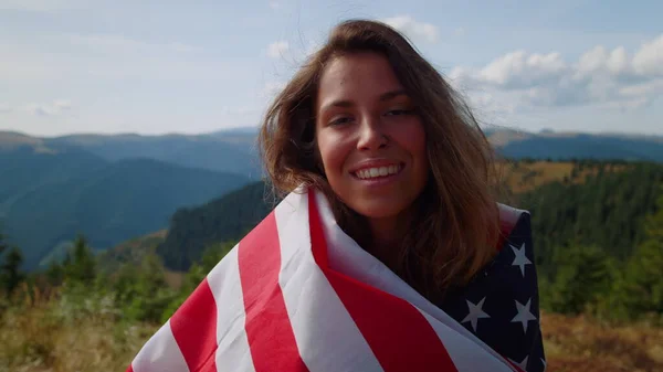 Woman with american flag standing in mountains. Tourist holding flag in hands