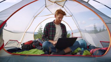 Turist çadırında dizüstü bilgisayarda çalışan bir adam. Dizüstü bilgisayarda yazan serbest çalışan erkek.
