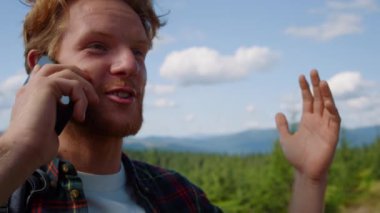 Dağlarda akıllı telefondan konuşan bir turist. Duygusal adam el hareketi yapıyor.