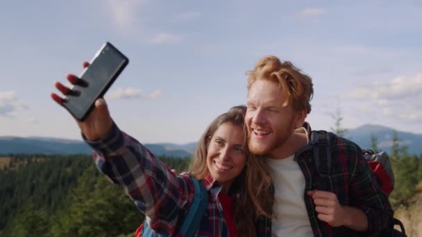 Positive woman and man taking selfie on smartphone during hike in mountains — Stock Video