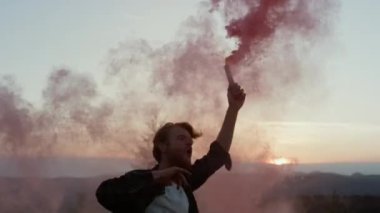 Gün batımında dağlarda dans eden adam. Heyecanlı adam aktif sis bombası tutuyor. 