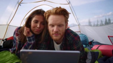 Odaklanmış kadın ve erkek çadırdaki tablet bilgisayarda film izliyorlar.