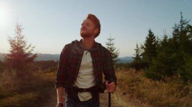 Yolda yürüyen memnun bir adam. Gülümseyen adam yürüyüş sopası kullanıyor.