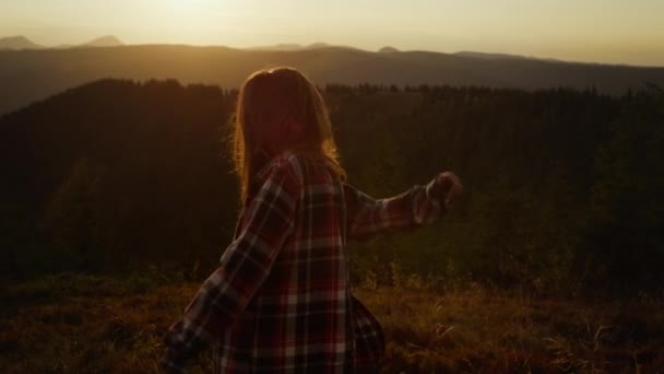 Захоплена дівчина танцює в горах на заході сонця. Жінка обертається на лузі — стокове відео