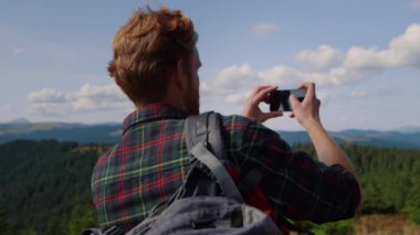 Akıllı telefonlu bir adam dağın tepesinde duruyor. Panoramik fotoğraf yapan adam