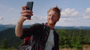 Yürüyüşçü dağlarda akıllı telefondan selfie çekiyor. Barış işareti gösteren adam 
