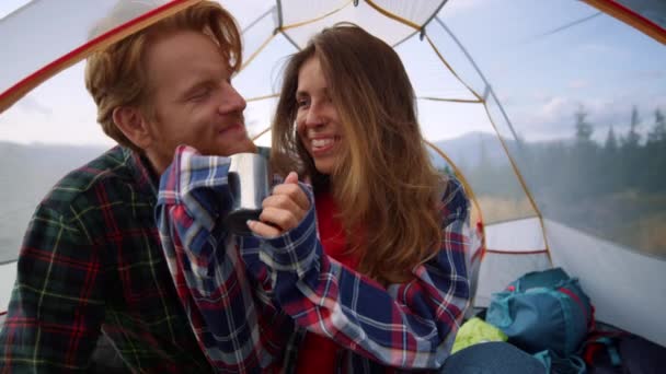 キャンプ中に観光テントに座っているハイカーカップル。男性と女性がお茶を飲む — ストック動画