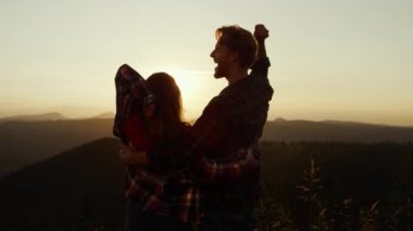 Dağlarda birbirini kucaklayan bir çift. Heyecanlı erkek ve kadın el kaldırıyor