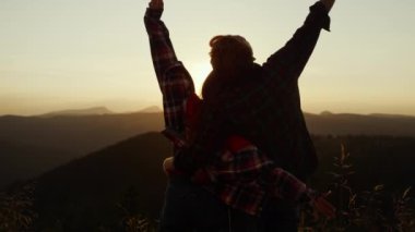 Dağda gün batımına bakan bir çift. Mutlu kadın ve erkek el kaldırıyor.