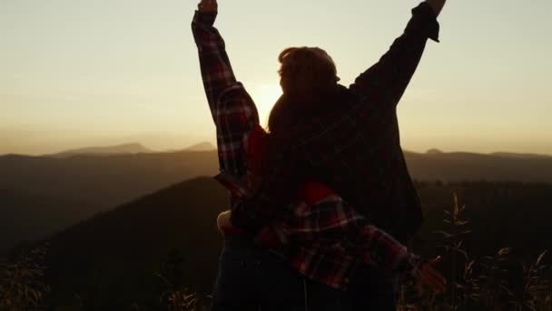 Beberapa melihat matahari terbenam di atas gunung. Wanita bahagia dan pria mengangkat tangan di udara — Stok Video