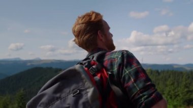 Sırt çantalı bir adam dağlarda yürüyor. Erkek yürüyüşçü dağın tepesinde duruyor.