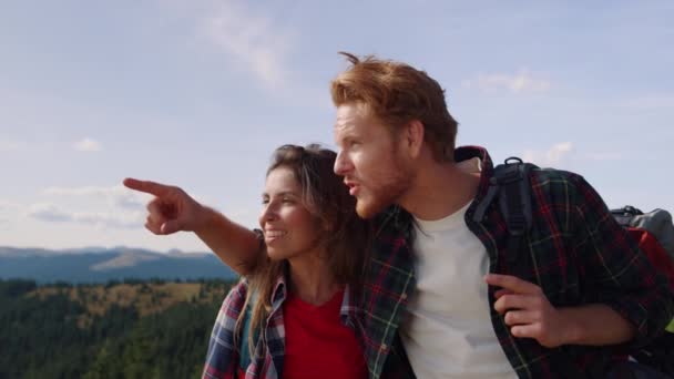 Woman and man standing on top of mountain. Male hiker pointing finger away — Stock Video
