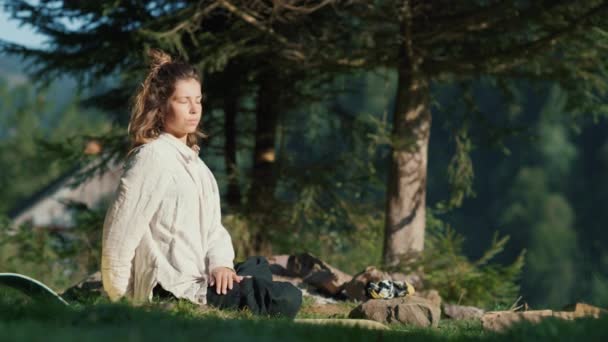 Ελκυστική κοπέλα που απολαμβάνει τη γιόγκα στα βουνά. Γιόγκα γυναίκα κάθεται στο γρασίδι. — Αρχείο Βίντεο