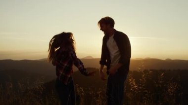 Gülümseyen kadın ve erkek gün batımında dağın tepesinde dans ediyorlar.