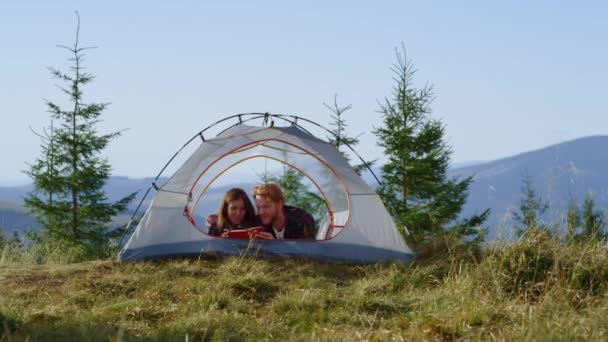 ハイキング中にテントに寝そべっているカップル。女と男がノートにメモを取る — ストック動画