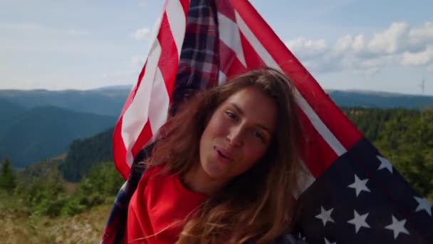 Дівчинка з американським прапором розважається в горах. Посміхнена жінка махає нам прапором. — стокове відео