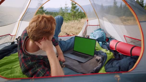 Seriös kille tittar på film på bärbar dator med grön skärm i tält — Stockvideo