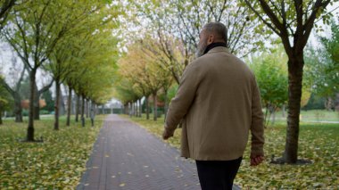 Sonbaharda güzel bir parkta yürüyen arka manzara adamı. Üst düzey arka görünüm.