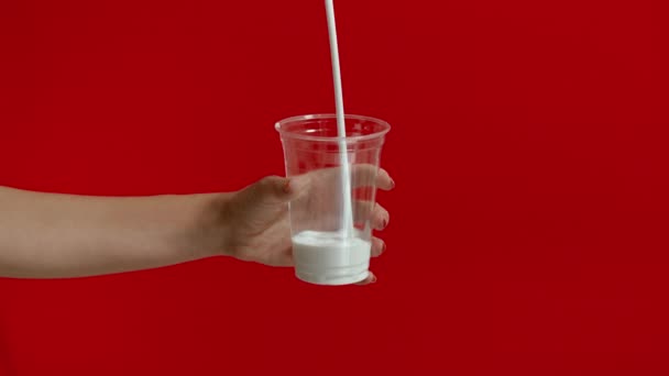 Breed uitzicht op de handen van de vrouw gieten melk in lege plastic glas in slow motion. — Stockvideo