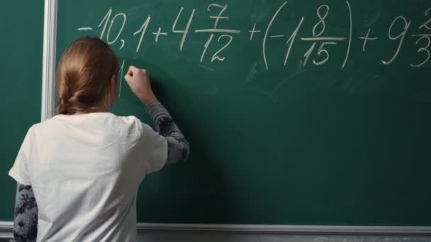 Back view of school girl doing math task on blackboard in class.Student writing — Stock Video