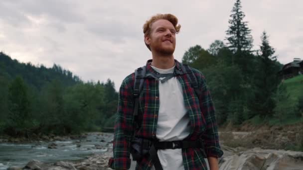 Turista caminando por el río. Sonriente hombre de pie junto al río de montaña — Vídeos de Stock