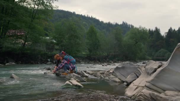 Senderistas tocando el agua en el río. Pareja positiva salpicando agua con las manos — Vídeo de stock