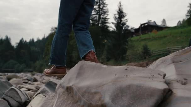 L'uomo con gli stivali che cammina sulle rocce al fiume. Escursionista di sesso maschile a piedi nelle montagne estive — Video Stock