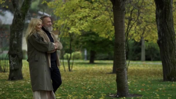 Foto lateral de hermosa pareja de ancianos caminando lentamente a lo largo del camino en el parque de otoño. — Vídeo de stock