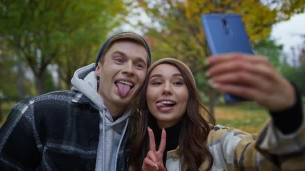 Positivos amantes jóvenes haciendo caras divertidas en selfie al aire libre. Pareja tomando fotos — Vídeos de Stock