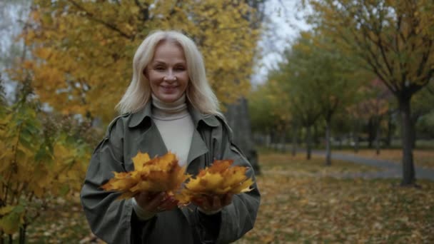 Großaufnahme glückliche ältere Dame hat Spaß mit Laub im Herbstpark in Zeitlupe — Stockvideo