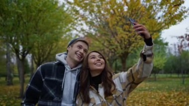 Sonbahar parkında cep telefonlarıyla selfie çeken komik genç bir çift..