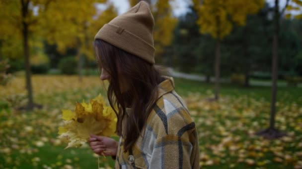 Side portrait of smiling attractive girl walking with yellow leaves in hands. — Stock Video