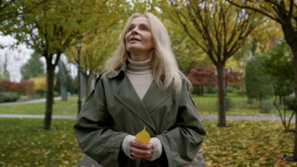 Retrato de una hermosa mujer caminando en el parque de otoño. Anciana sosteniendo hojas — Vídeo de stock