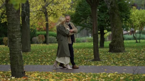 Side view shot of beautiful happy lovers walking along path among autumn trees. — Stock Video