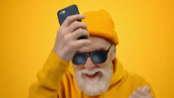 Aged man holding cellphone indoors. Carefree guy moving hands in studio. — Stock Photo, Image