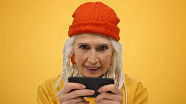 Mulher idosa alegre comemorando dentro de casa. Senhora excitada jogando no telefone no estúdio. — Fotografia de Stock