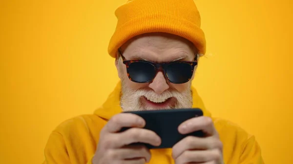 Пожилой человек жестикулирует в помещении. Счастливый парень играет на мобильном телефоне в студии. — стоковое фото