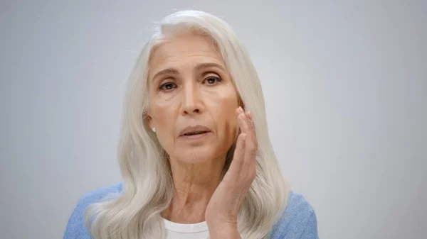 Ontspannen vrouw die binnenshuis voor haar gezicht zorgt. Senior dame strelen huid binnen. — Stockfoto