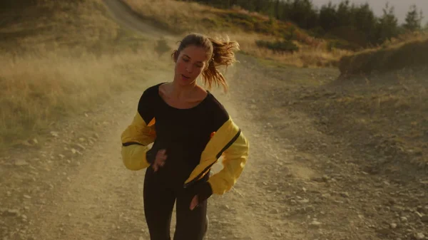 Vermoeide atleet joggen op vuile weg. Meisje in sportkleding loopt in de bergen — Stockfoto