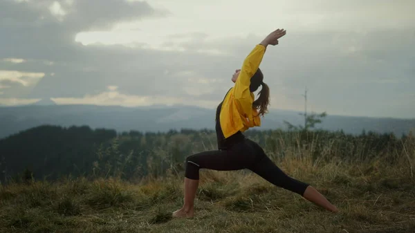 A jógás nő harcos pózban áll. Fitt lány meditál a hegyekben — Stock Fotó