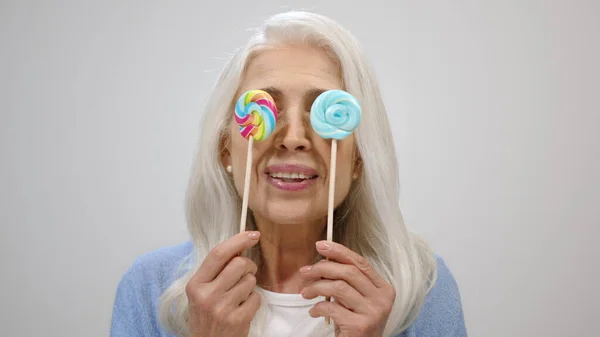 Vieja alegre sosteniendo caramelos en el estudio. Feliz anciana divirtiéndose en interiores. — Foto de Stock