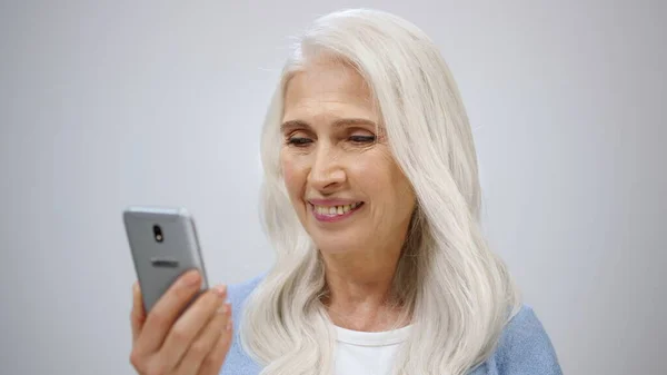 Ηλικιωμένη γυναίκα που ψάχνει σε εσωτερικούς χώρους. Ώριμη κυρία βλέποντας ειδήσεις στο κινητό. — Φωτογραφία Αρχείου