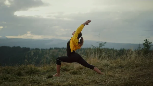 Yoga woman doing warrior pose in mountains. Flexible girl practicing yoga